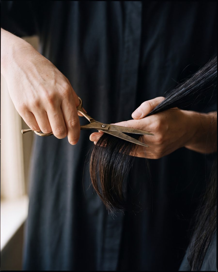 A stylist's hands cutting a section of hair with shears.